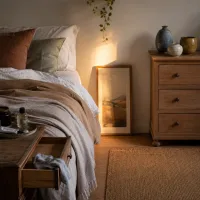 Wide view of the small bedroom at dusk, showing dresser, nightstand, and bed.