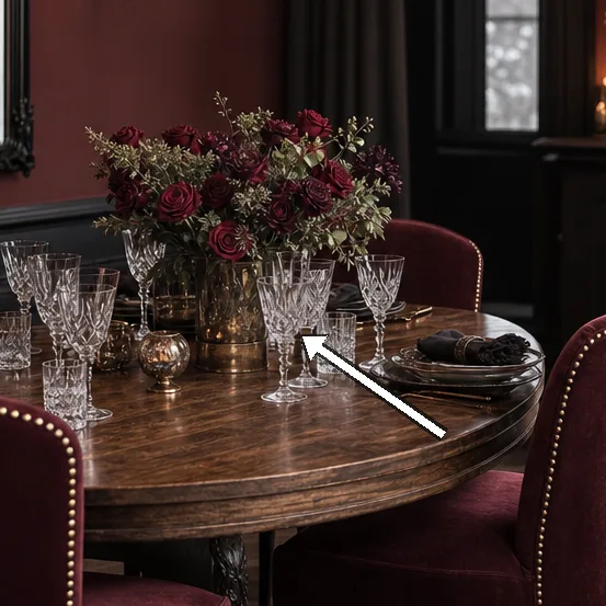 Round wooden table crowned by glassware and a floral arrangement.